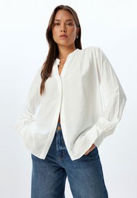 Witte blouse met lange mouwen, ontspannen pasvorm, textuurstof. Gepaard met blauwe spijkerbroek, toont een casual look.