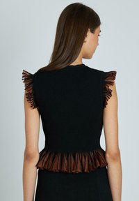 Top sin mangas negro acanalado con flecos marrones en los hombros y un dobladillo de peplum. La textura parece suave y elástica.