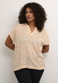 Blouse ample à manches courtes en tissu léger, de couleur blanche avec un motif abstrait orange et jaune et un décolleté en V.