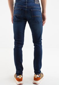 Temno modre skinny jeans iz denima z diskretnim rumenim šivom, ki imajo dva zadnja žepa z zigzag obliko in logotipni pečat na pasu.