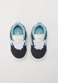 Schwarz und blaue Stoff-Sneaker mit weißen Schnürsenkeln, einer weißen Zunge und leichter blauer Akzentuierung an der Seite. Flache weiße Gummisohle.