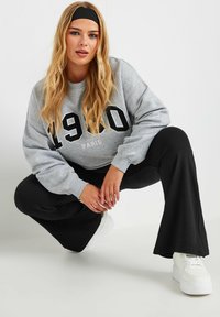 Harmaa huppari, jossa on "1990 PARIS" -grafiikka, yhdistettynä mustiin liehulegginseihin ja valkoisiin tennareihin. Mallilla on pitkät, laineikkaat hiukset ja musta pidike.