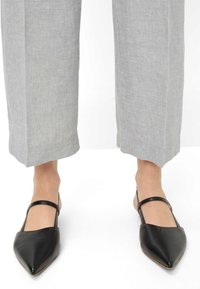 Zwarte pointy slingback schoenen van glad leer met een slanke enkelband. Draagt bij grijze linnen brede broek.