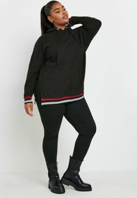 Svart hoodie med ribbade ärmar, med röda och grå ränder vid fållen. I kombination med svarta leggings och kraftiga svarta stövlar.