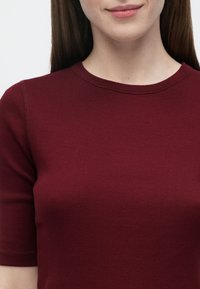 Vinrød ribbestrikket topp med korte ermer og rund hals, med glatt tekstur og subtile sømdetaljer.