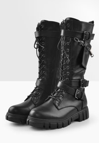 Botas altas de rodilla de piel sintética negra con cordones en la parte delantera, correas con hebillas, suelas gruesas y cremallera lateral para facilitar su uso.