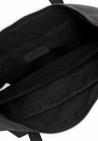 Interior de bolso de tela negra con compartimento con cremallera, que cuenta con múltiples bolsillos y una etiqueta de marca. Textura suave en general.