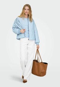 Veste matelassée bleu clair portée sur un pull assorti, accompagnée d'un pantalon blanc à jambes larges et d'un sac cabas en cuir marron. Les accessoires notables incluent des chaussures pointues.