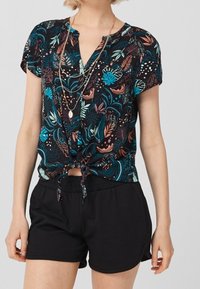 Blusa a maniche corte con sfondo nero e motivo floreale colorato. Dettaglio a nodo in vita abbinato a pantaloni corti neri.