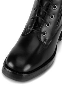 Melna ādas potīšu zābaks ar noapaļotu pirkstu, saistāmu priekšpusi, metāla acīm un sānu rāvējslēdzēju. Spīdīga apdare ar izturīgu papēdi un zoli.