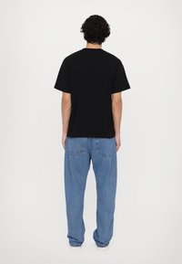 Svart bomulls t-skjorte med korte ermer, rund hals og løs passform, sammen med lyseblå denimjeans med baklommer.