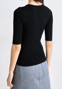 Top negro de punto con mangas cortas y escote redondeado. Diseño ajustado que acentúa la cintura, la textura parece suave y elástica.