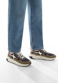 Sneakers neri e verde oliva con logo a stella bianco, pannelli texturizzati e accenti beige. Presentano una suola bianca spessa e ammortizzata.