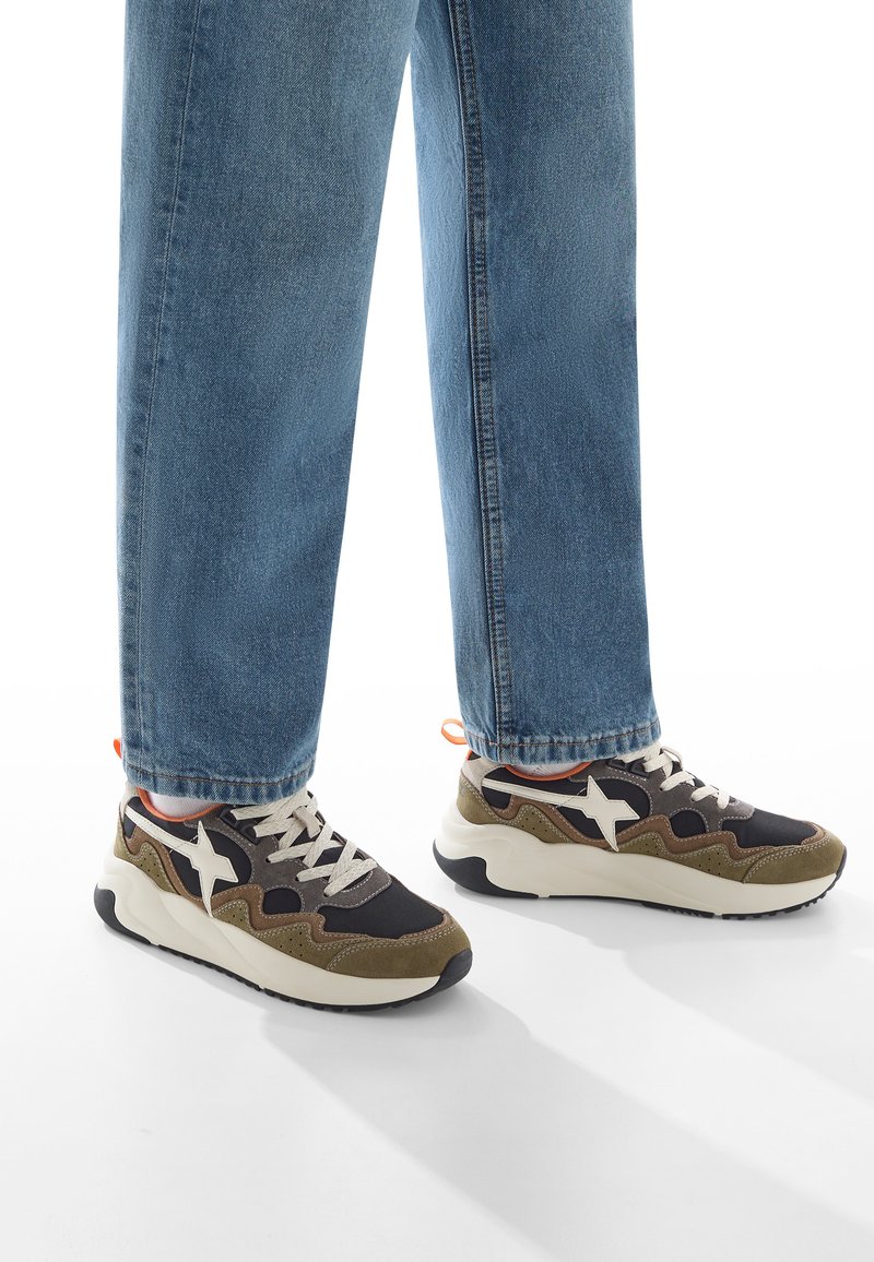 Sneakers neri e verde oliva con logo a stella bianco, pannelli texturizzati e accenti beige. Presentano una suola bianca spessa e ammortizzata.