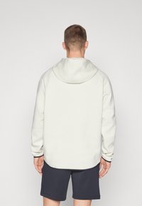Hellgrauer Hoodie mit Kordelzugkapuze, gerippten Bündchen und Saum. Kombiniert mit dunkelblauen Shorts, die einen lockeren Schnitt und eine glatte Textur aufweisen.