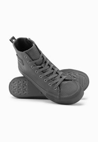 Zapatillas altas de goma gris oscuro, con un diseño texturizado, cordones y una puntera de goma a rayas en contraste.