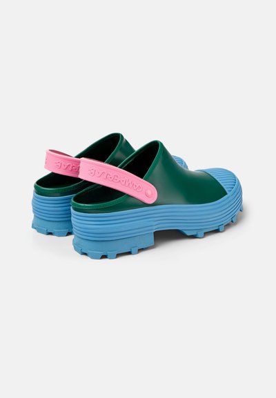 Zoccoli in gomma verdi con un cinturino rosa sul tallone e suola blu rigata. Presentano un design texturizzato e una suola spessa per una buona aderenza.