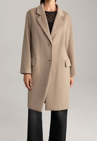 Béžový vlněný kabát s klopovým límcem, jednořadým zapínáním na knoflíky a dvěma předními kapsami. Hladká textura a mírně volný střih.