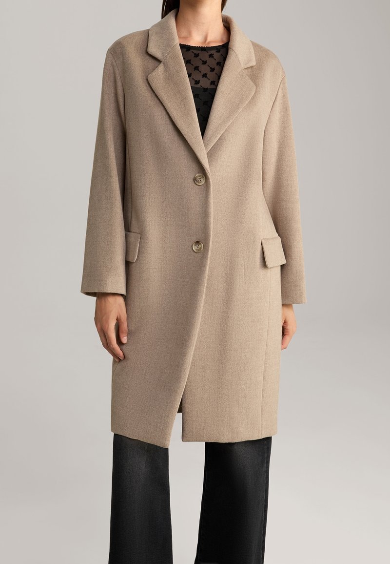 Béžový vlněný kabát s klopovým límcem, jednořadým zapínáním na knoflíky a dvěma předními kapsami. Hladká textura a mírně volný střih.