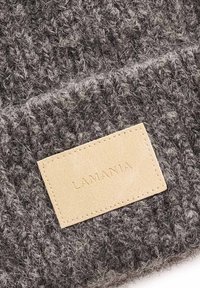 Căciulă gri tricotată din lână, cu textură moale și o patch de piele bej cu textul în relief „LAMANIA”.