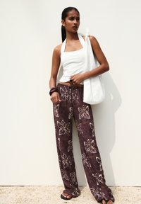 Top bianco a collare e pantaloni larghi viola con stampa floreale. Tessuto testurizzato, abbinato a una borsa bianca con motivo. Sandali neri piatti.