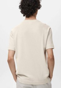 Beige kortærmet skjorte med et struktureret strikkemønster og rund hals. Bagsiden har en afslappet pasform og subtile ribbede detaljer ved ærmerne.
