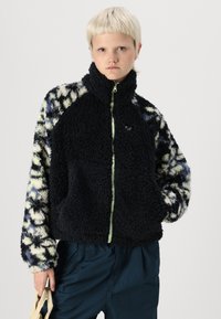 Chaqueta de forro polar con un cuerpo negro, mangas con un estampado en azul y crema, cierre completo con un acento y un diseño de cuello alto.