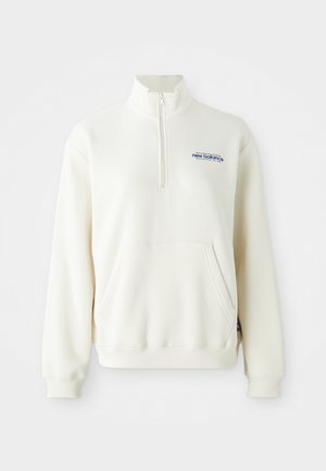 Sweatshirt crème avec col zippé, poche avant, poignets côtelés et logo "new balance" en bleu sur la poitrine. Texture douce.