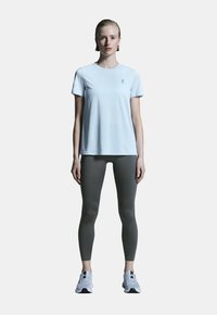 Ljusblå kortärmad träningsskjorta, kombinerad med figurformade grå leggings och grå löparskor. Enkel design, slät textur.