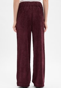 Pantalons larges en velours côtelé bordeaux avec une taille élastique, présentant une texture côtelée verticale et une coupe décontractée.