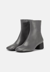 Botas de tobillo de cuero gris con una textura suave, cierre de cremallera y un tacón bajo y redondeado. Presentan un diseño minimalista con costuras ordenadas.