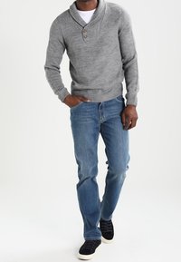 Pull gris en tricot avec col châle et trois boutons, associé à un jean en denim bleu et des baskets noires, présentant une texture lisse.