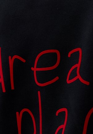 Vue partielle d'un tissu noir avec de grandes lettres minuscules rouges imprimées dessus.