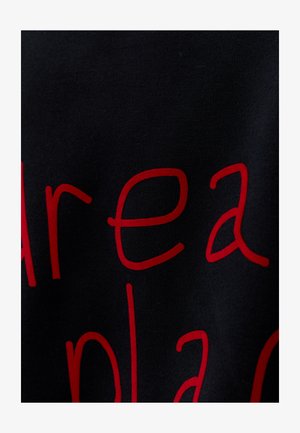 Vue partielle d'un tissu noir avec de grandes lettres minuscules rouges imprimées dessus.