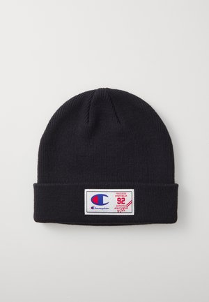 Beanie en tricot noir avec un revers replié. Le patch logo sur le devant présente un logo bleu et rouge avec du texte. Le matériau semble doux et extensible.