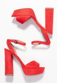 Des sandales à talons hauts en suède rouge disposent d'une large plateforme, d'une bride ajustable à la cheville et d'un talon épais avec une finition lisse.