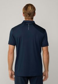 Navy sininen polo-paita lyhyillä hihoilla, kauluksella ja logotiedoilla takana. Sujuva pinta, muotoiltu istuvuus. Takakuvan esitys.