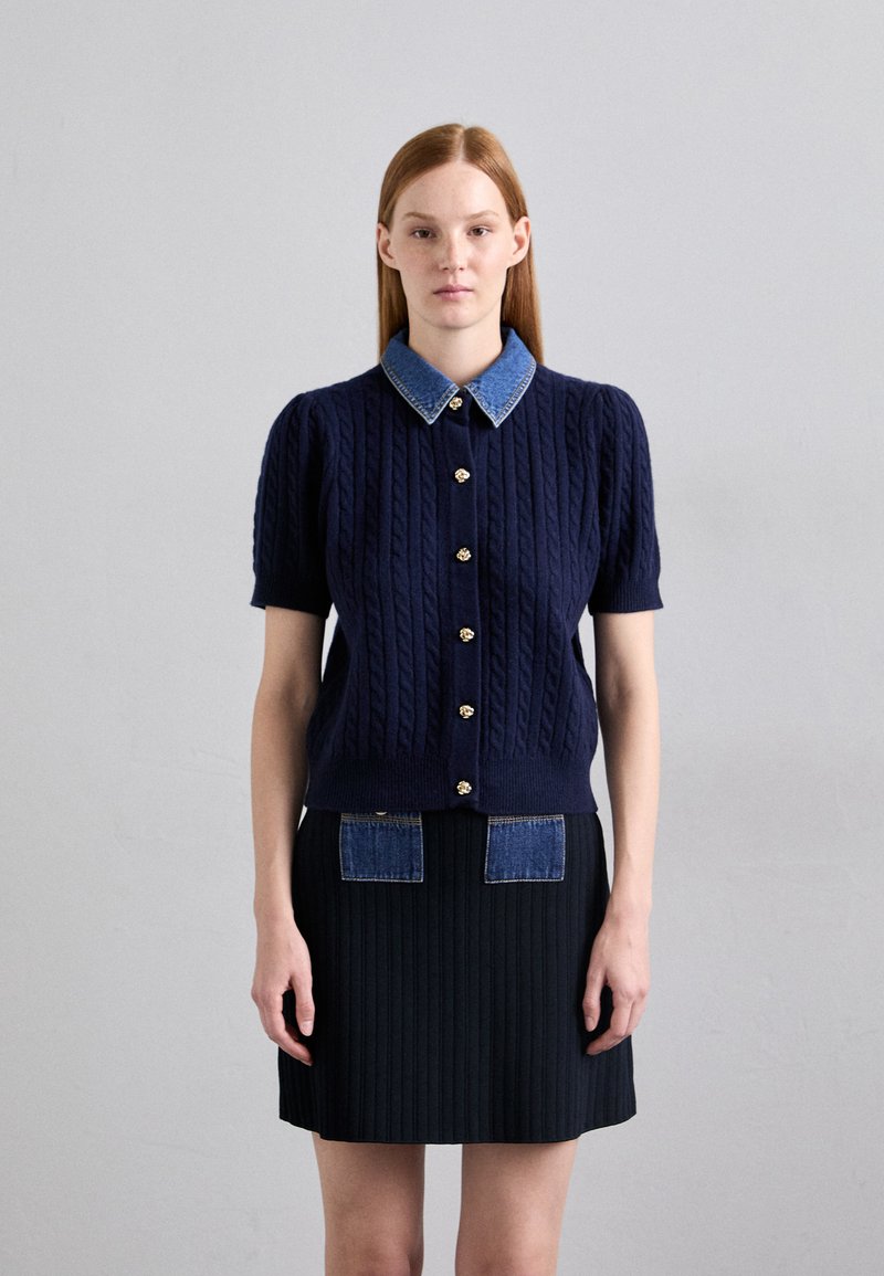 Navy cable-knit cardigan with short sleeves, denim collar, and gold button accents. Paired with a ribbed black skirt featuring denim pockets.