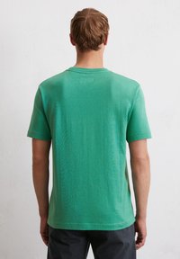 T-shirt vert à manches courtes en tissu doux. Modèle classique à col rond avec une texture unie, sans motifs ni logos visibles au dos.