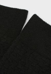 Calze nere lavorate a maglia con un motivo testurizzato lungo il bordo e un design a costine. Il materiale sembra morbido con una finitura liscia.