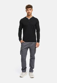 Sort langærmet henley-shirt med hvid kravekant, kombineret med grå cargobukser med sidelommer og løs pasform.
