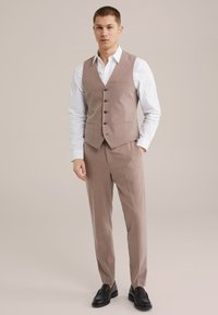 Hellbraunes maßgeschneidertes Anzug mit einer taillierten Weste, weißem Hemd und schwarzen Schuhen. Die Weste hat eine Fünf-Knopf-Verschluss und seitliche Taschen.