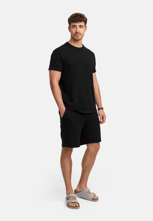 Camiseta negra texturizada y pantalones cortos a juego, combinados con sandalias grises. El conjunto presenta un ajuste relajado y bolsillos laterales.