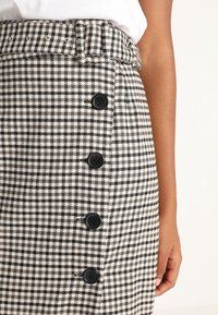 Falda a cuadros en blanco y negro con cintura ajustada, que cuenta con seis botones negros en la parte delantera y una tela texturizada.