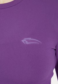 Dopasowany, fioletowy top z długim rękawem wykonany z gładkiego, elastycznego materiału. Posiada subtelne szare logo na klatce piersiowej oraz okrągły dekolt.