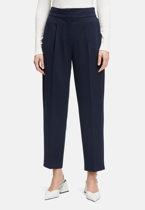 Marineblauwe, hoogwaardig broek met een geplooid ontwerp, gemaakt van soepele stof. Korte lengte met een rechte pasvorm, gecombineerd met witte blokhak-schoenen.