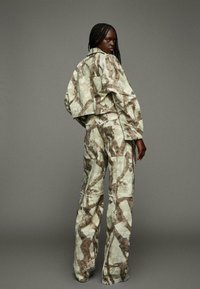 Geknipte, oversized jas en brede broek in een camouflagepatroon met aardetinten. Bevat grote zakken en heeft een ontspannen pasvorm. Getextureerde stof.