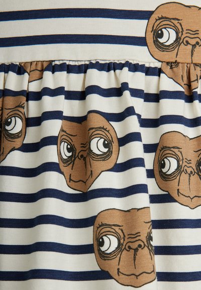 Juostuota medžiaga su kreminėmis ir tamsiai mėlynomis linijomis, kurioje pavaizduotos kelios animacinių filmų stiliaus ateivio veidai. Audinys yra švelnus ir susiraukšlėjęs liemens srityje.