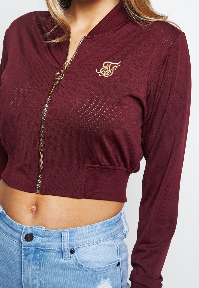 Bordowy, krótki zamek błyskawiczny z teksturowanej tkaniny, z długimi rękawami i złotym, haftowanym logo na piersi.