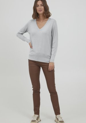Maglione grigio chiaro a V con maniche lunghe, abbinato a pantaloni slim-fit marroni. Sneakers con suola testurizzata completano l'outfit.